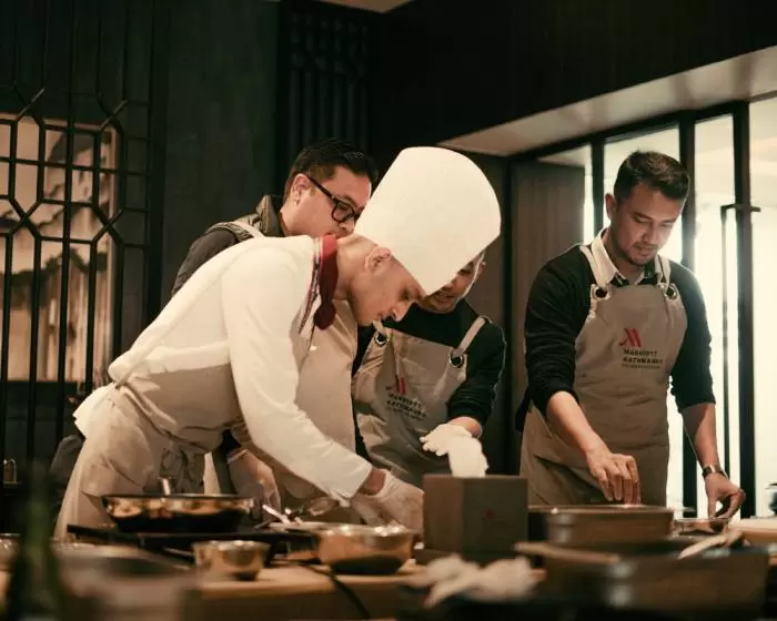 cooks leaning over a commercial kitchen stove